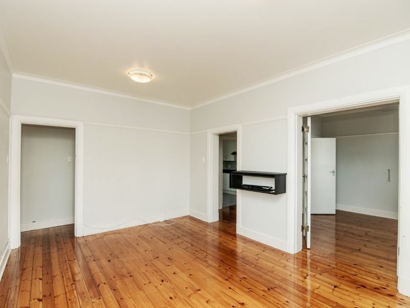 A bright, empty living room featuring polished timber flooring, classic architraves, and neutral wall finishes, offering a versatile space for interior design.