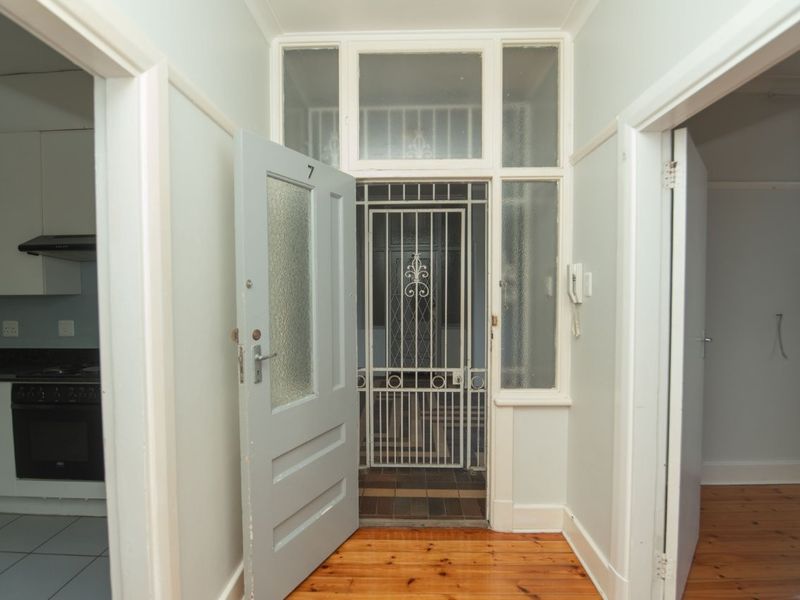 Entrance hallway featuring timber flooring, a security gate, and an intercom system, providing access to the adjacent kitchen and living areas.