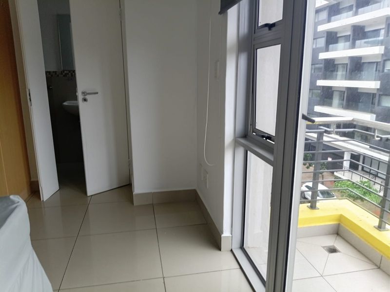 A bright, empty bedroom featuring tiled flooring, large aluminium windows, and direct access to a private balcony.
