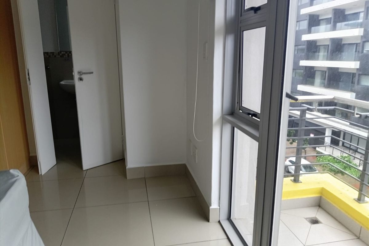 A bright, empty bedroom featuring tiled flooring, large aluminium windows, and direct access to a private balcony.