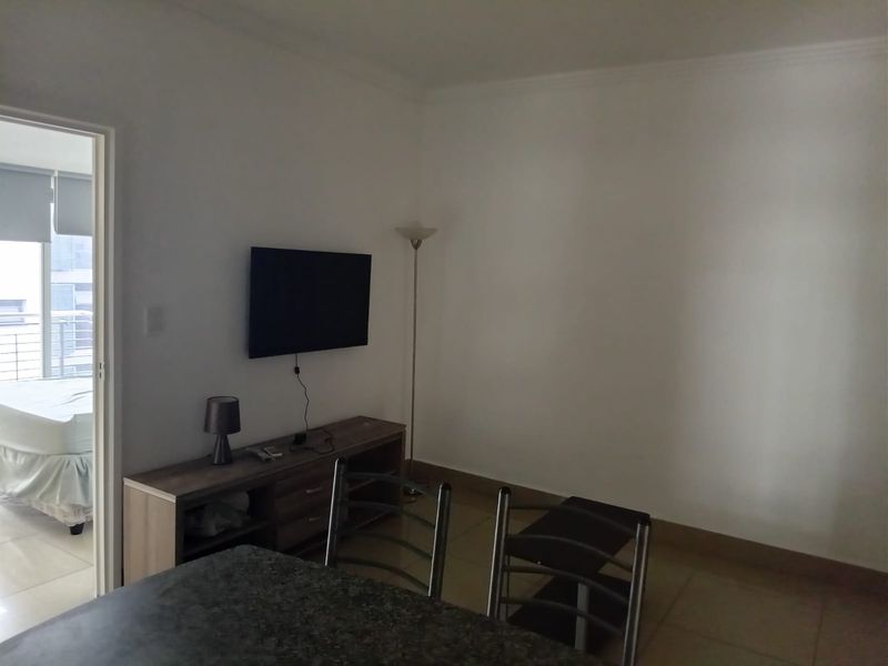 A living area featuring tiled flooring and coving, with a view into an adjacent bedroom.