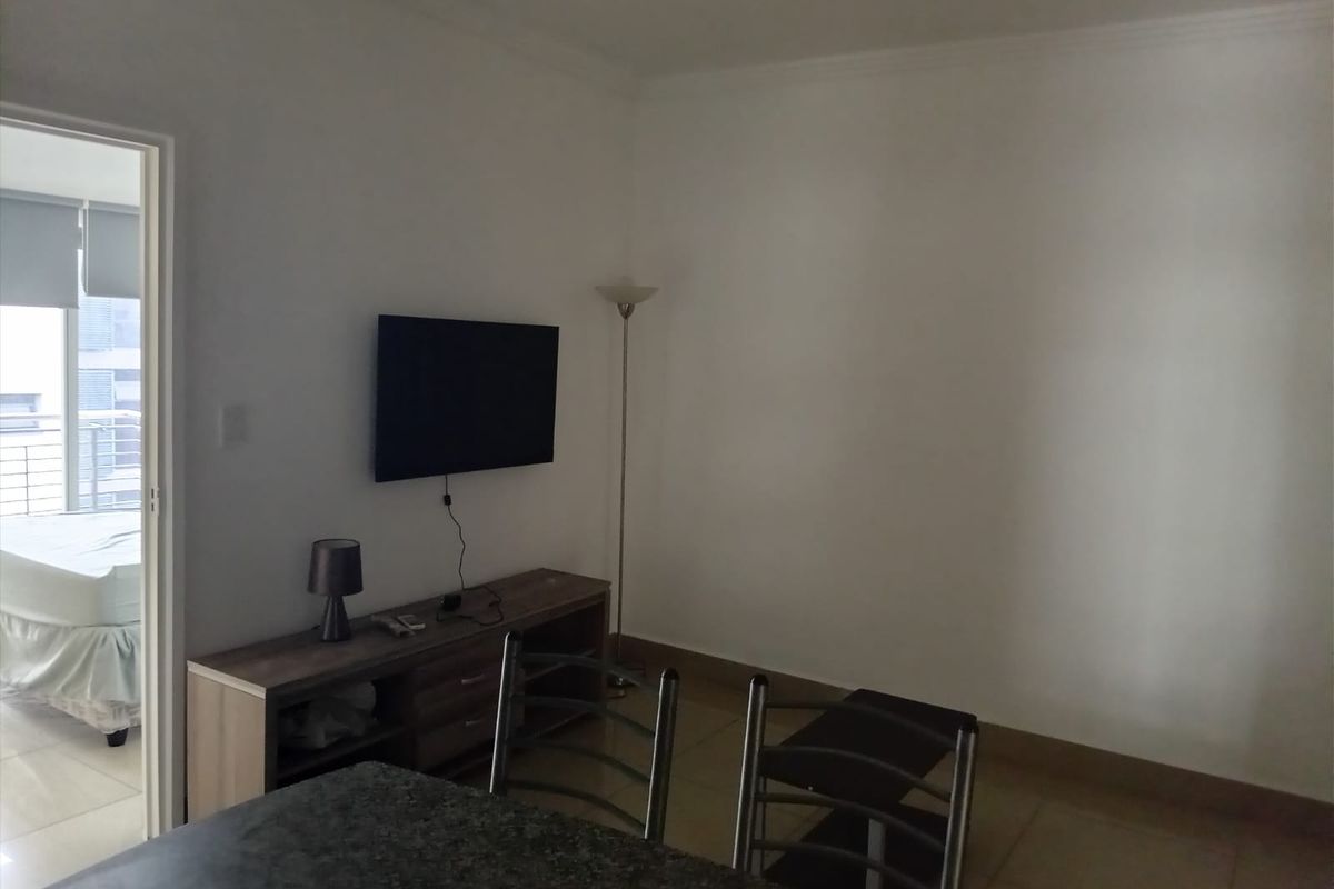 A living area featuring tiled flooring and coving, with a view into an adjacent bedroom.