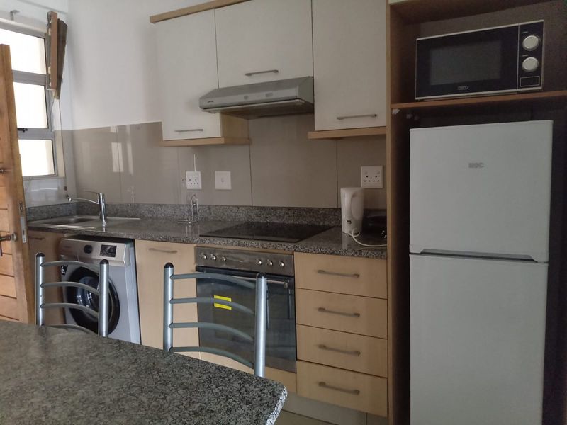 Compact kitchen featuring granite countertops, built-in oven, electric hob, extractor fan, and integrated cabinetry with a tiled splashback.