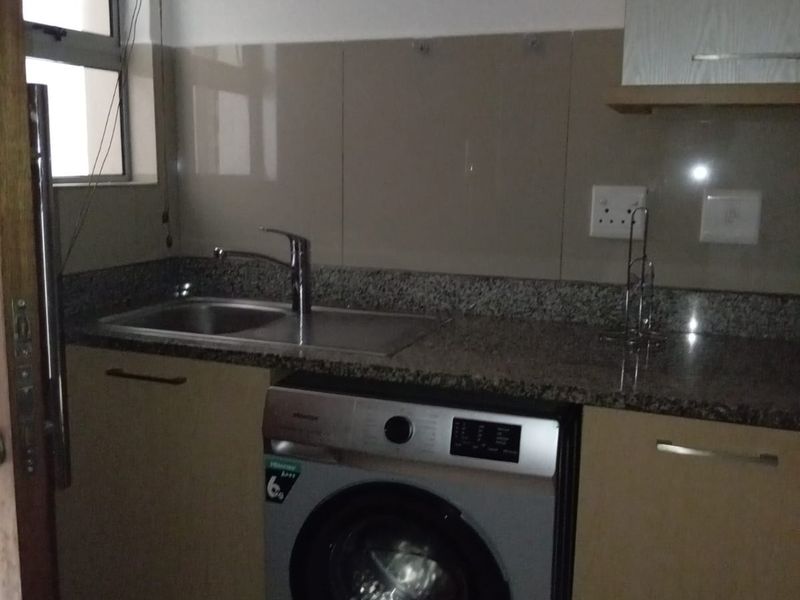Compact laundry area featuring granite countertops, built-in cabinetry, a stainless steel sink, and tiled splashback, providing functional utility space.