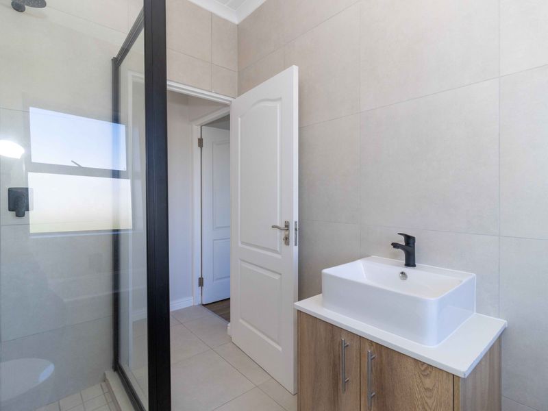 Modern bathroom featuring a vessel sink with a black faucet, vanity cabinet, and a walk-in shower with a black-framed glass enclosure.