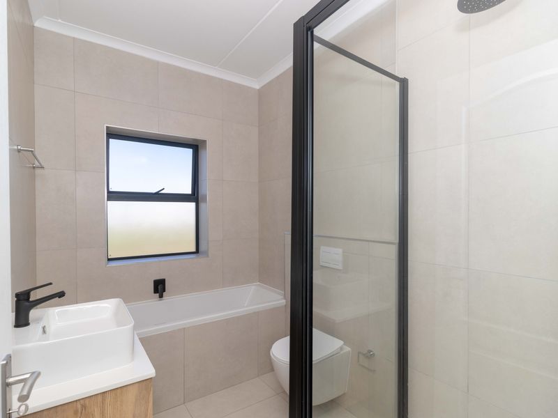 Modern bathroom featuring a built-in bathtub, wall-mounted toilet, glass-enclosed shower, and a contemporary vessel sink with black fixtures.