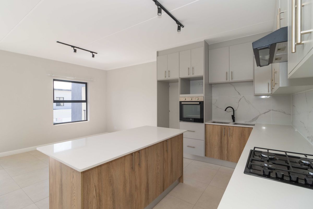 Modern open-plan kitchen featuring a central island, built-in oven, gas hob, and contemporary cabinetry with marble-look splashbacks and sleek track lighting.