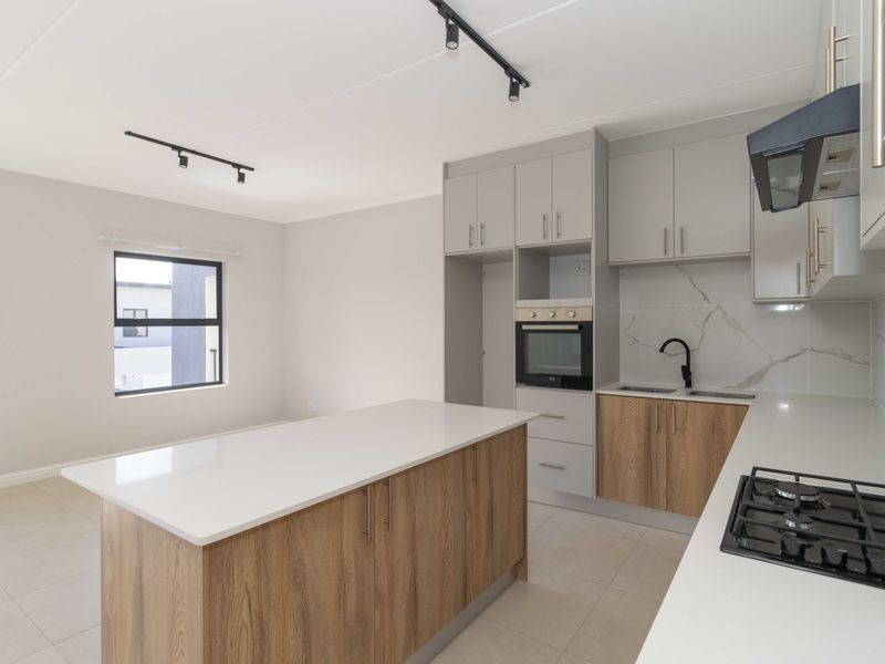 Modern open-plan kitchen featuring a central island, built-in oven, gas hob, and contemporary cabinetry with marble-look splashbacks and sleek track lighting.