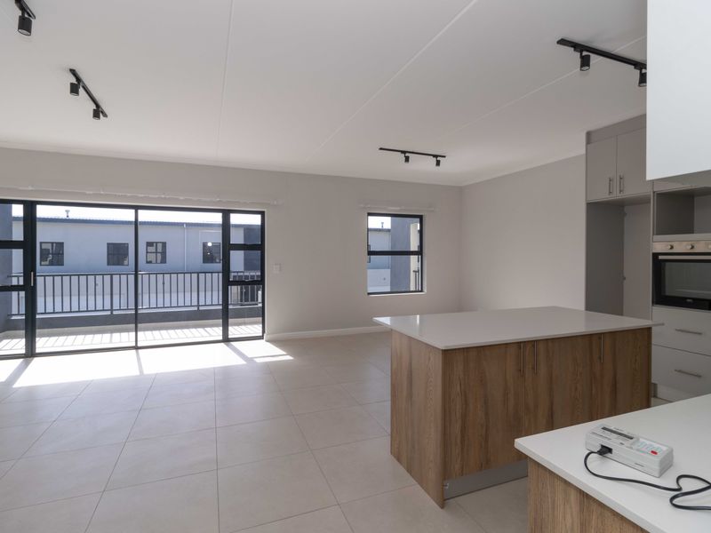 Modern open-plan living area featuring a kitchen island, built-in oven, sleek cabinetry, and large sliding doors leading to a balcony.