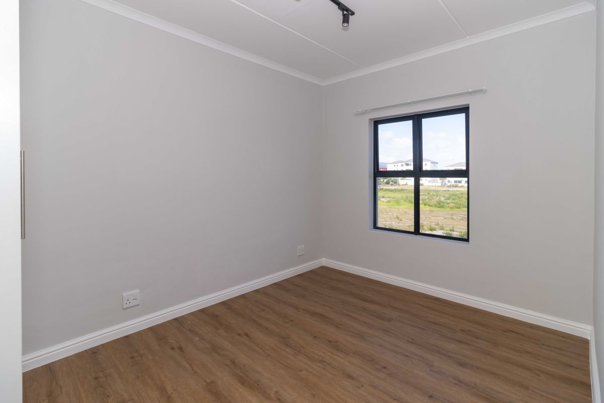 A clean, empty bedroom featuring modern laminate flooring, neutral walls, and a large window with views of the surrounding area.