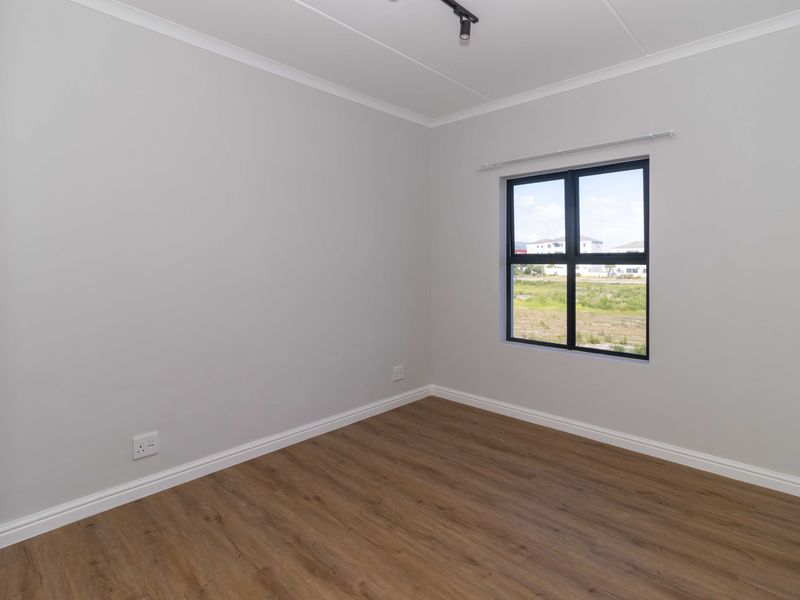 A clean, empty bedroom featuring modern laminate flooring, neutral walls, and a large window with views of the surrounding area.