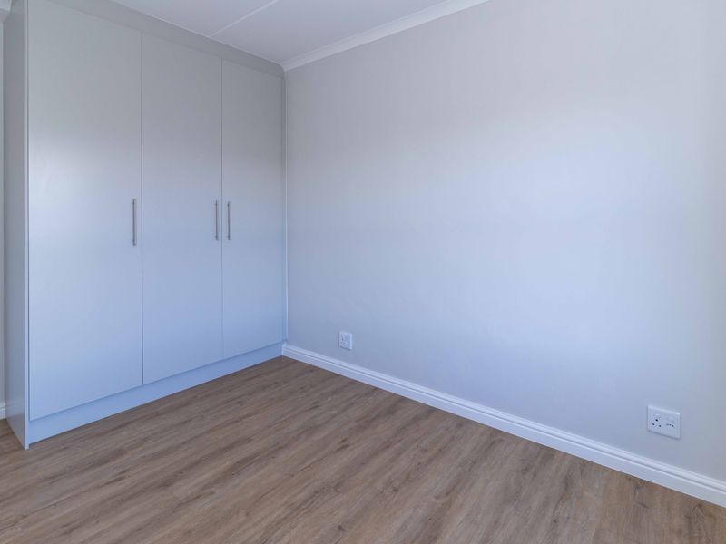 A clean, empty bedroom featuring modern laminate flooring and neutral-toned built-in cupboards, offering a versatile space ready for personalization.