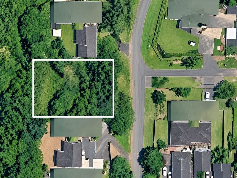 An aerial view of a residential neighborhood showing a vacant plot of land highlighted within a white border, surrounded by established homes and trees.