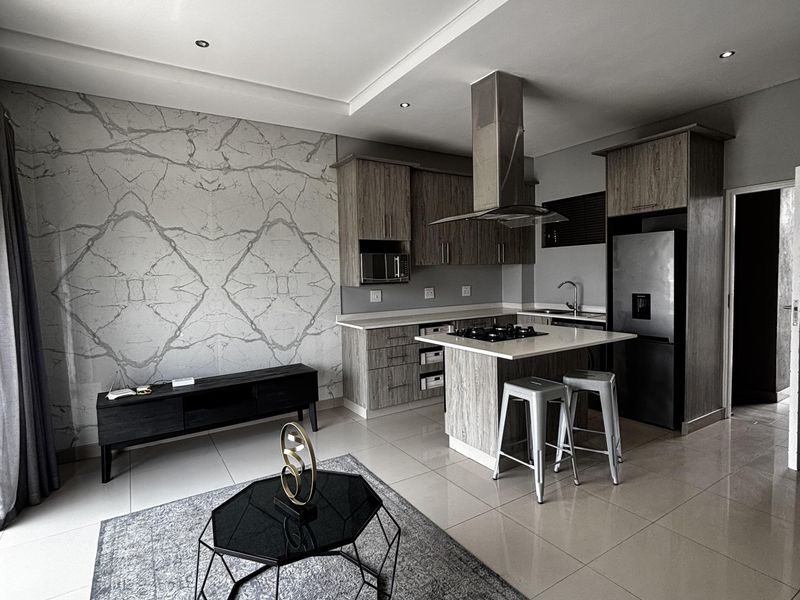 Modern open-plan living area featuring a sleek kitchen with island, gas hob, extractor fan, and a striking marble-effect feature wall.