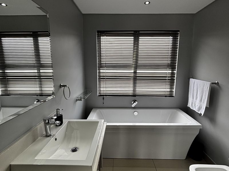 Modern bathroom featuring a sleek freestanding bathtub, contemporary vanity with basin, bidet, and high-quality finishes including recessed lighting and venetian blinds.