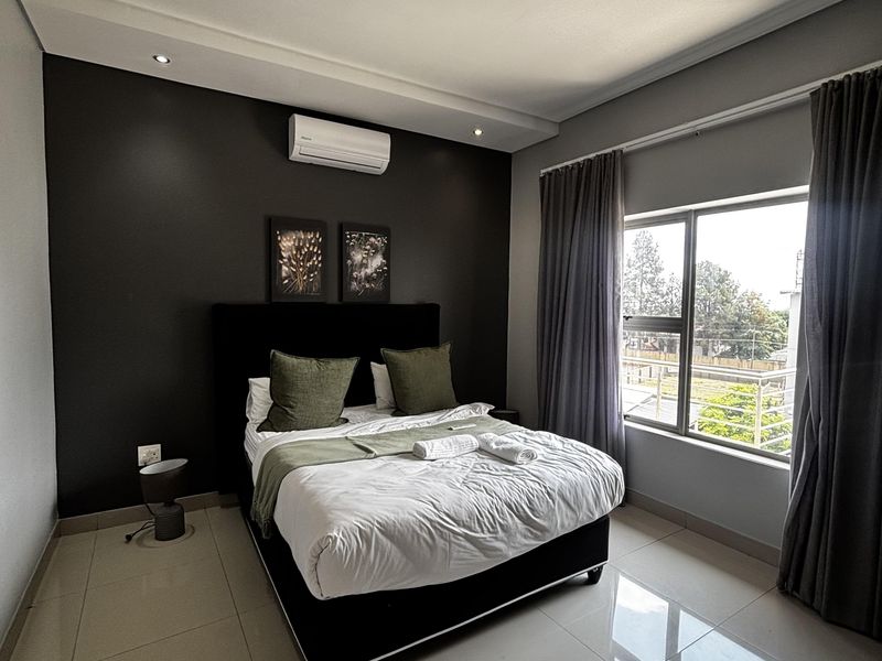 A modern bedroom featuring tiled flooring, a dark accent wall, recessed ceiling lighting, and an integrated air conditioning unit.