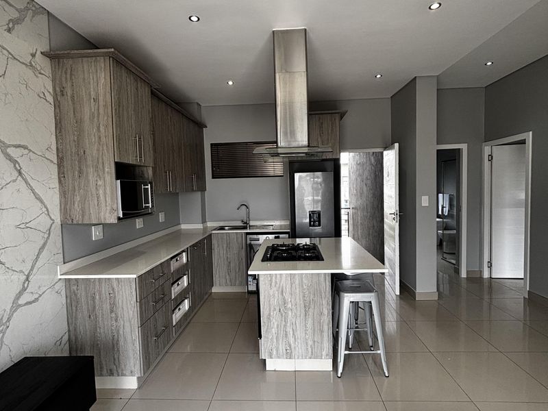 Modern kitchen featuring wood-grain cabinetry, stone countertops, a central island with a gas cooktop, and a striking marble-effect feature wall.