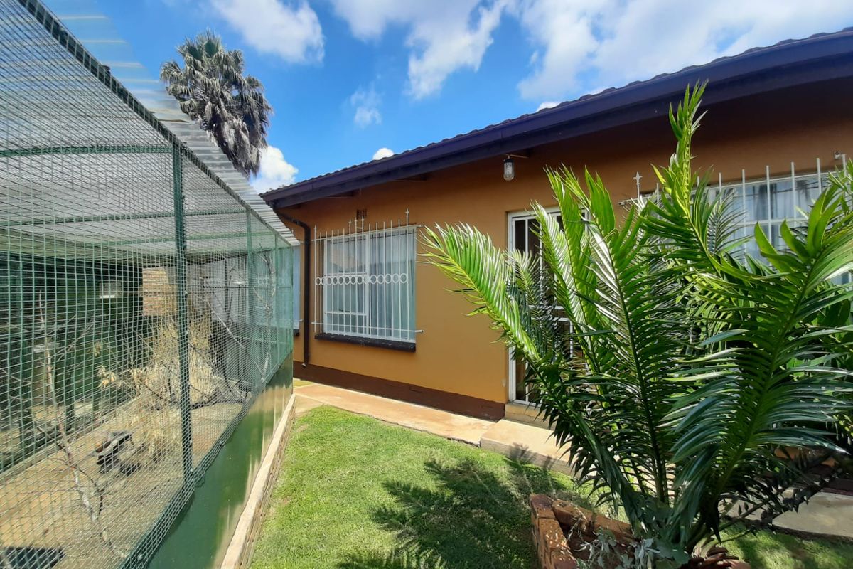 Rear exterior view of the house featuring a lawn, concrete pathway, security bars on windows, and a large outdoor enclosure.