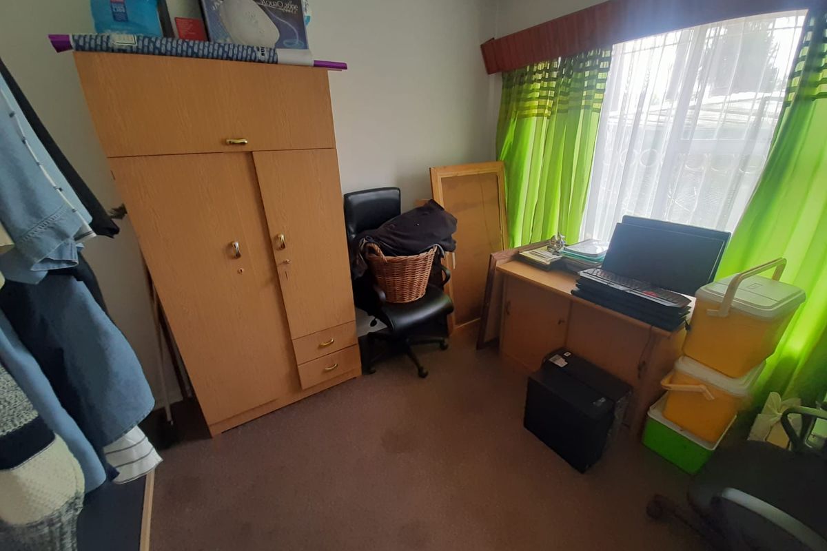 A bedroom featuring carpeted flooring and a window with a pelmet, currently utilized as a storage and workspace area.