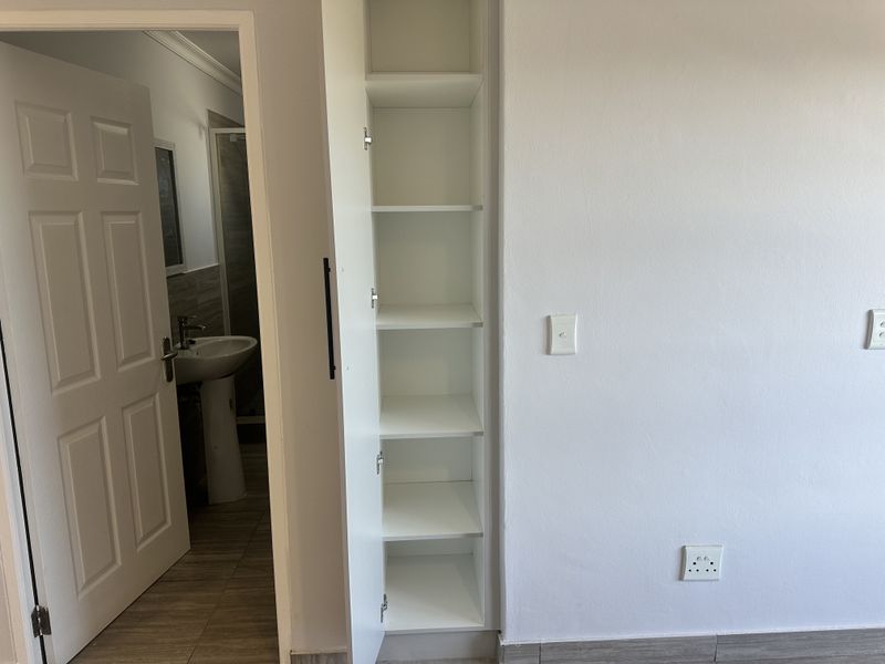 A clean bedroom interior featuring built-in shelving and direct access to an en-suite bathroom with a pedestal basin.
