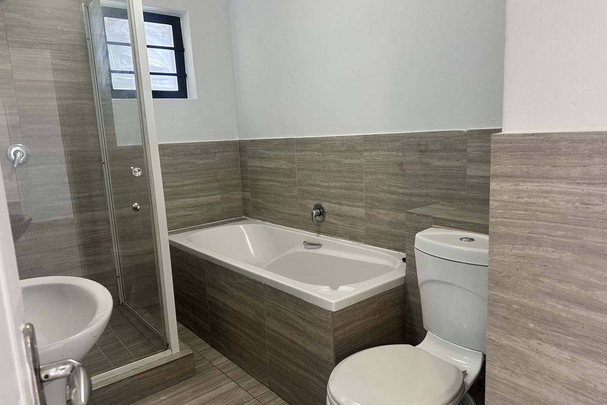 A modern bathroom featuring a built-in bathtub, a separate glass-enclosed shower, and a toilet, finished with neutral wood-look wall and floor tiles.