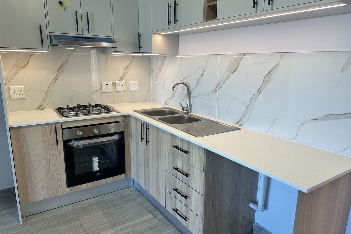 Modern kitchen featuring light wood cabinetry, quartz countertops, marble-look splashback, gas hob, built-in oven, and integrated under-cabinet lighting.