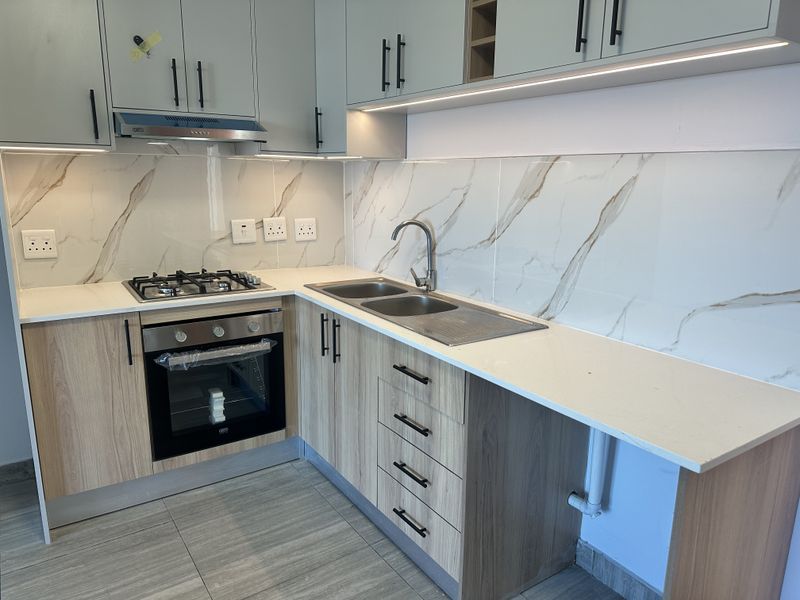 Modern kitchen featuring light wood cabinetry, quartz countertops, marble-look splashback, gas hob, built-in oven, and integrated under-cabinet lighting.
