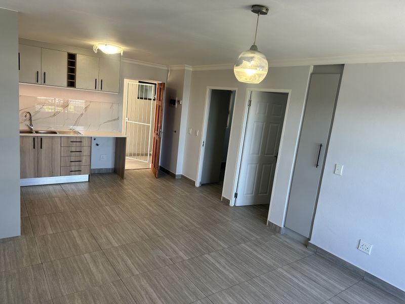 An open-plan living and kitchen area featuring modern wood-finish cabinetry, marble-look splashback, tiled flooring, and neutral wall tones.