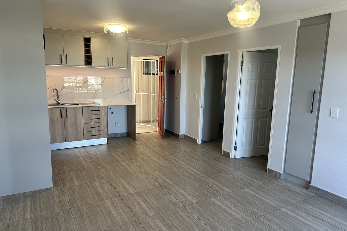 An open-plan living and kitchen area featuring modern cabinetry, marble-look backsplash, tiled flooring, and neutral finishes, providing a clean and versatile space.