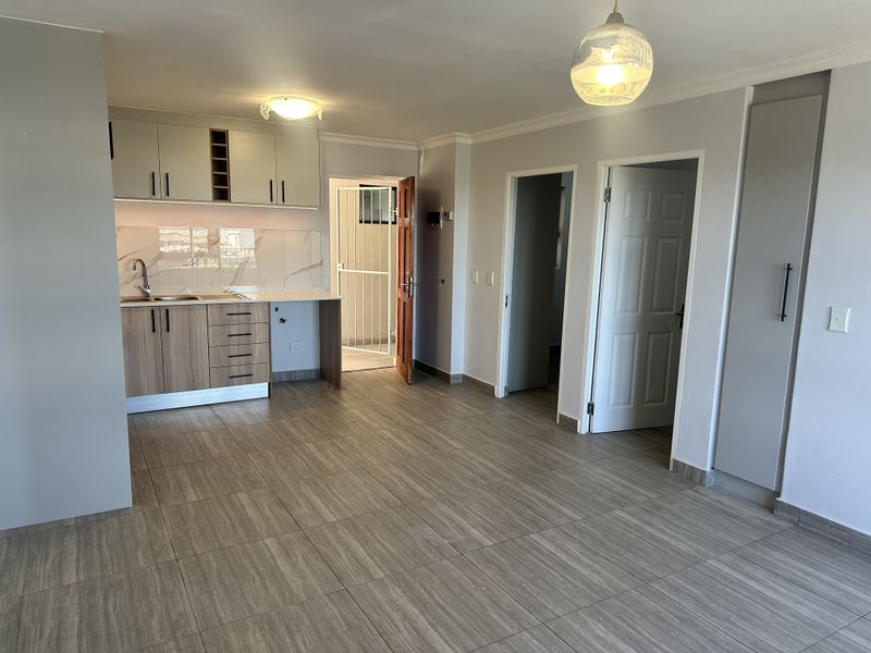 An open-plan living and kitchen area featuring modern cabinetry, marble-look backsplash, tiled flooring, and neutral finishes, providing a clean and versatile space.