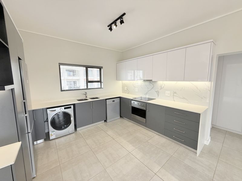 Modern kitchen featuring sleek grey and white cabinetry, stone countertops, marble-look splashback, integrated appliances, and contemporary track lighting.