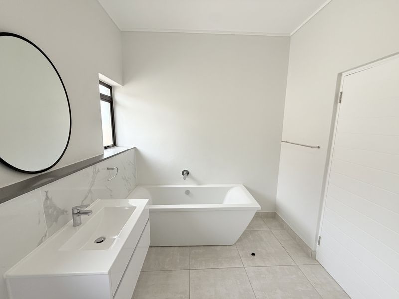 Modern bathroom featuring a sleek freestanding bathtub, wall-mounted basin with marble-look splashback, and neutral floor tiling in a clean, minimalist design.