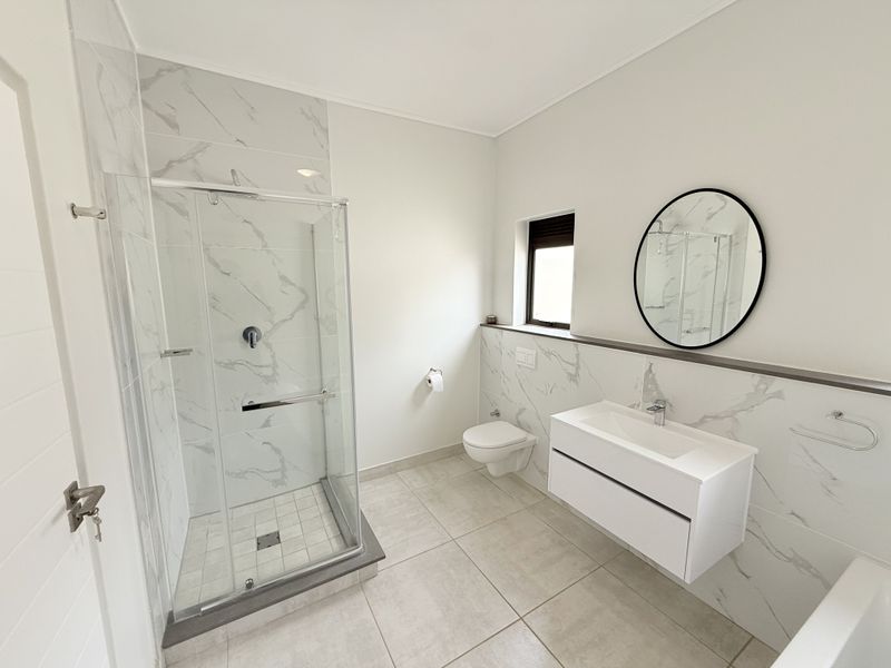 Modern bathroom featuring a glass shower enclosure, wall-mounted vanity, wall-hung toilet, and elegant marble-look wall tiling.