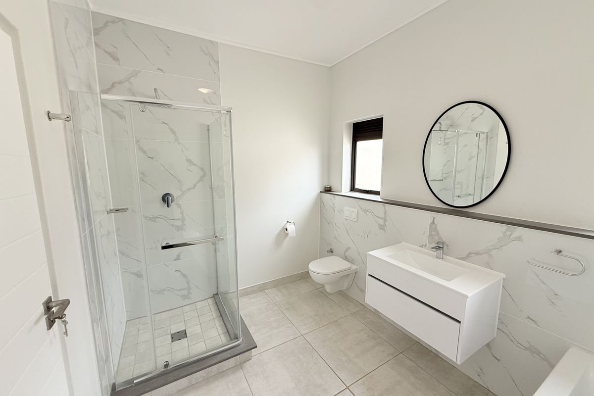 Modern bathroom featuring a glass shower enclosure, wall-mounted vanity, wall-hung toilet, and elegant marble-look wall tiling.