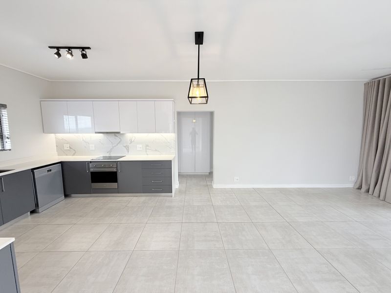 Modern open-plan kitchen and living area featuring sleek two-tone cabinetry, marble-look backsplash, integrated appliances, and neutral tiled flooring throughout.