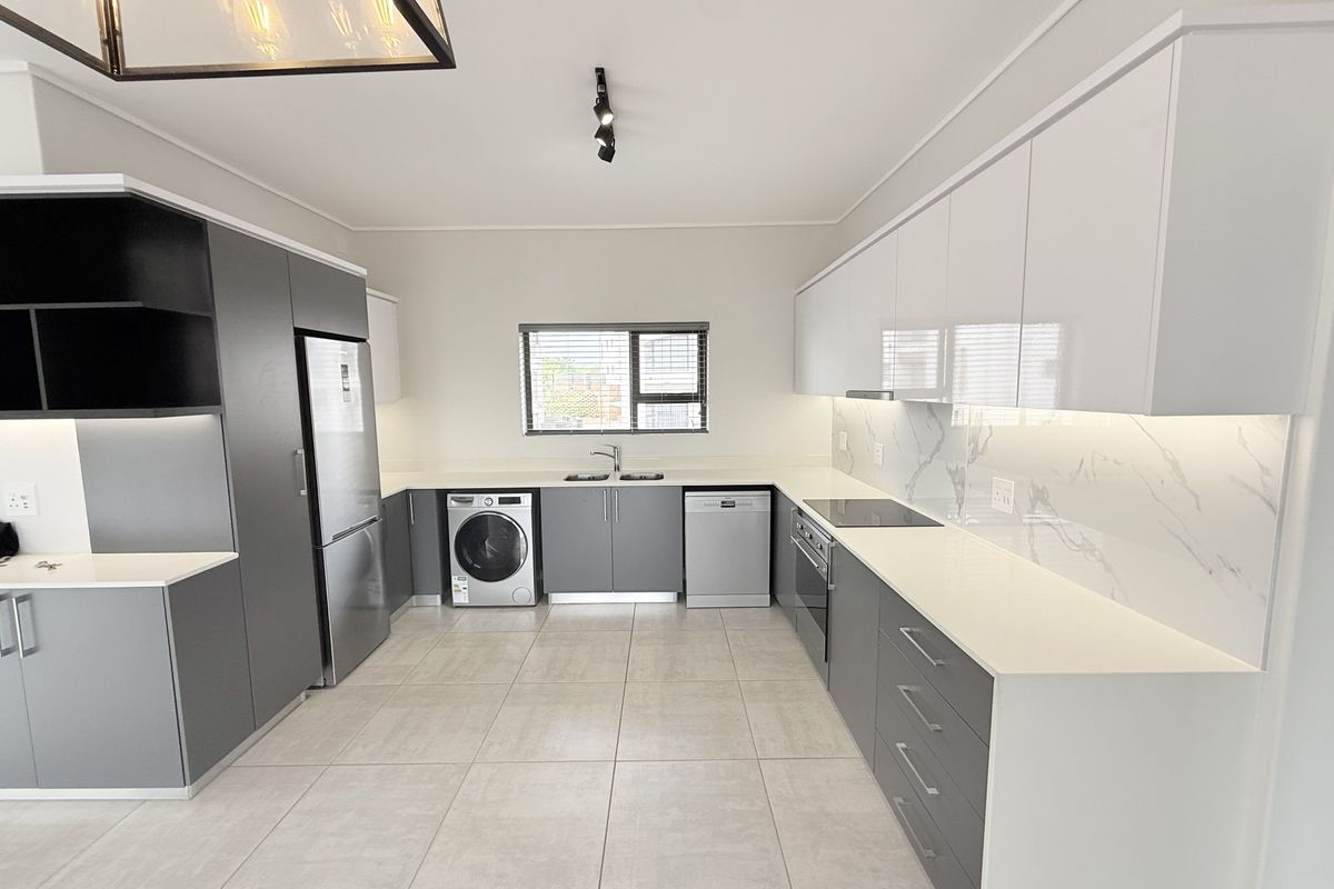 Modern kitchen featuring sleek grey and white cabinetry, stone countertops, marble-look splashback, and integrated appliances with high-quality finishes.