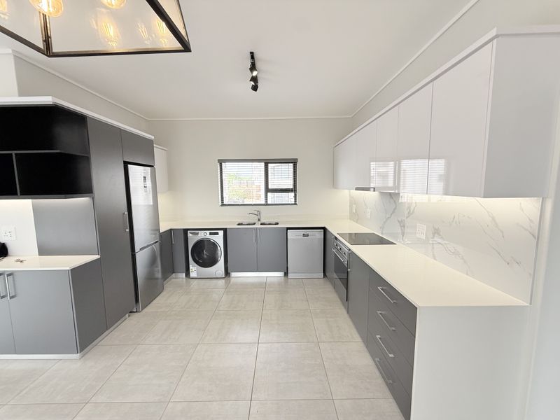 Modern kitchen featuring sleek grey and white cabinetry, stone countertops, marble-look splashback, and integrated appliances with high-quality finishes.