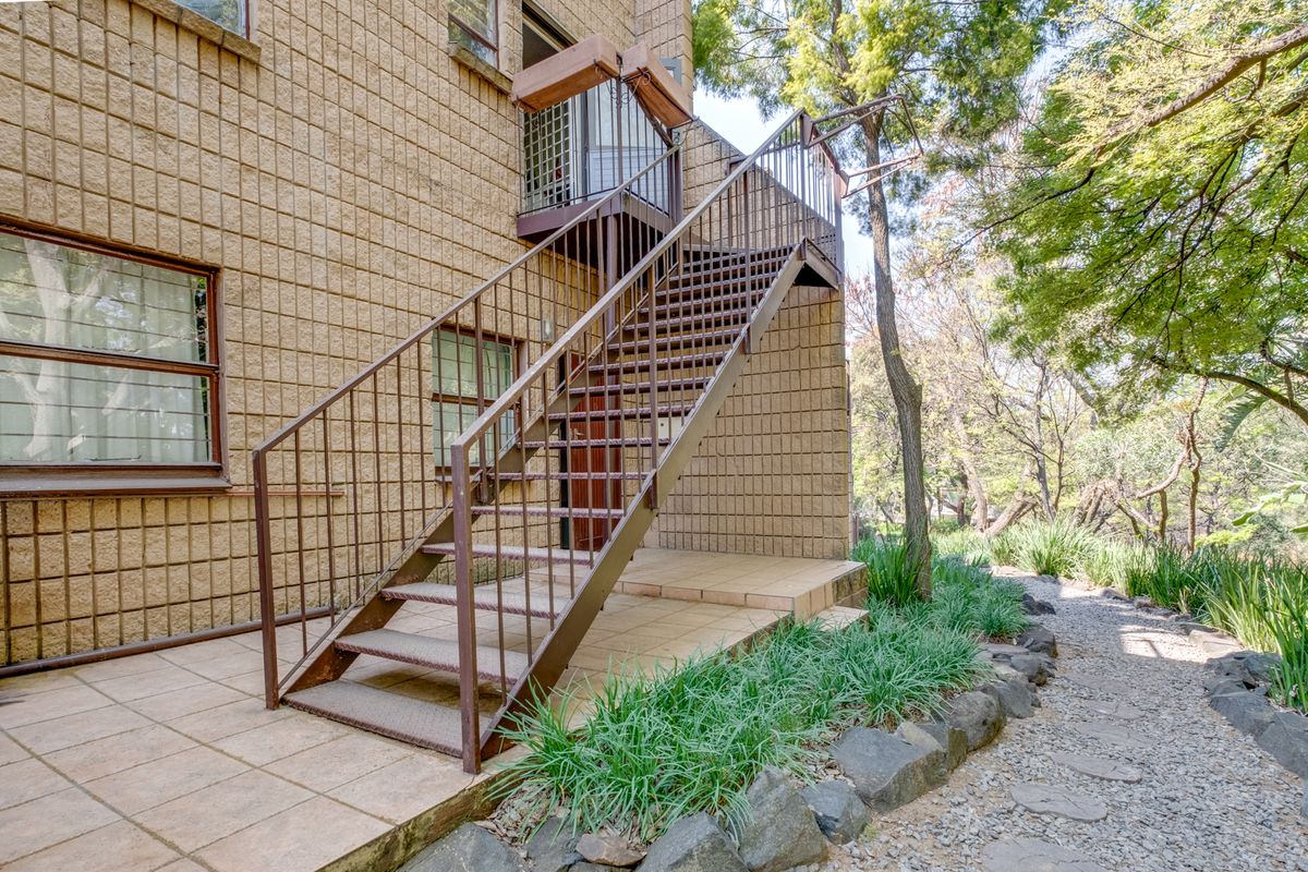 Exterior view of an apartment building featuring a metal staircase leading to an upper level, set against a landscaped garden and paved patio area.
