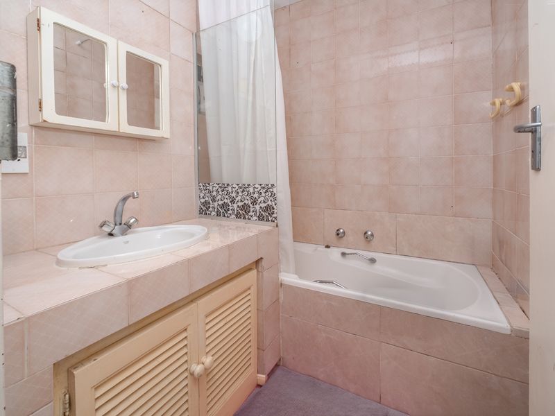 A dated bathroom featuring a built-in vanity with basin, a bathtub with shower mixer, and full-height wall tiling.