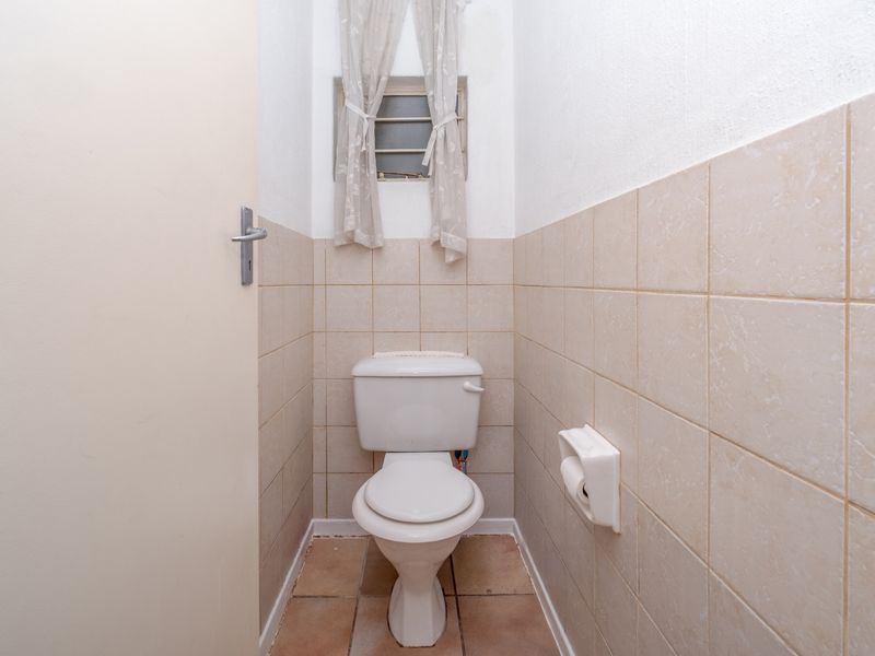 A compact guest toilet featuring neutral ceramic wall and floor tiles, a standard white toilet suite, and a small window for ventilation.