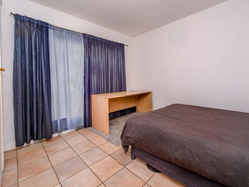 A bedroom featuring tiled flooring and a sliding glass door with curtains, providing access to the exterior.