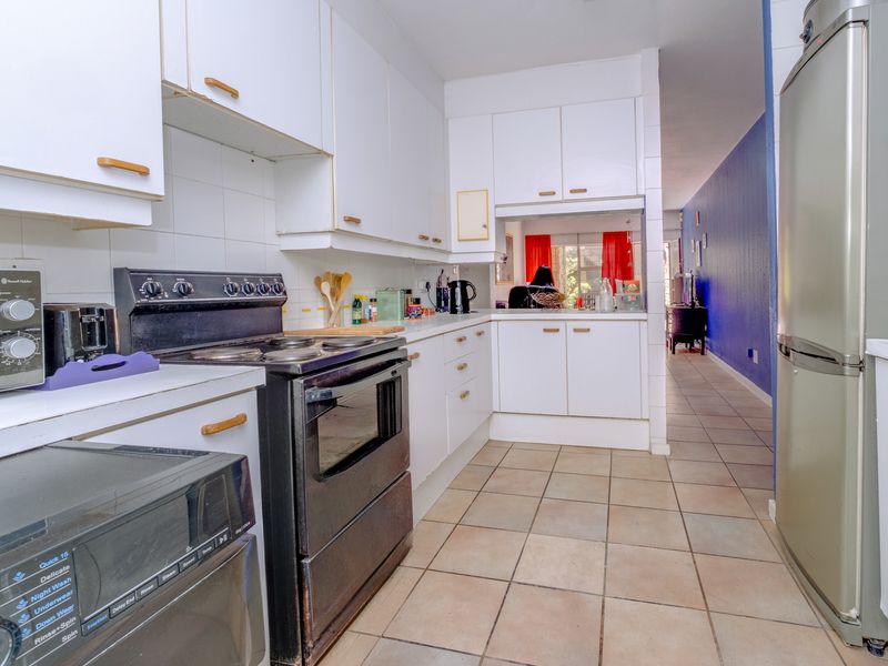 A functional kitchen featuring white cabinetry, tiled flooring, and a built-in electric stove, offering a practical layout with direct access to the hallway.