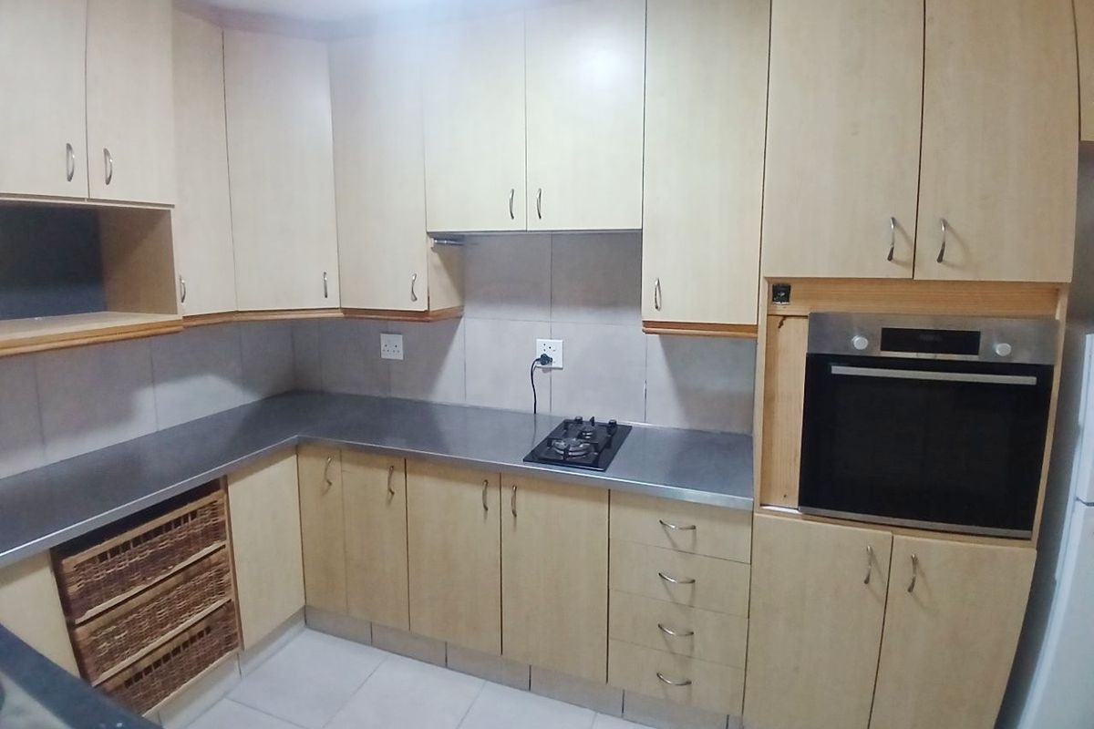 A functional kitchen featuring light wood-finish cabinetry, stainless steel countertops, a built-in oven, and a gas hob with tiled backsplash and flooring.