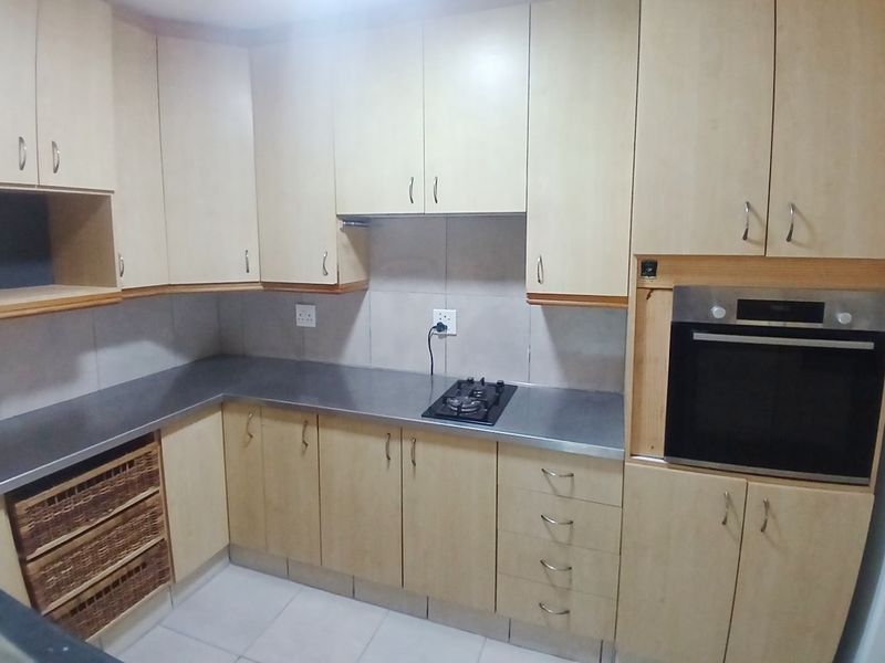 A functional kitchen featuring light wood-finish cabinetry, stainless steel countertops, a built-in oven, and a gas hob with tiled backsplash and flooring.