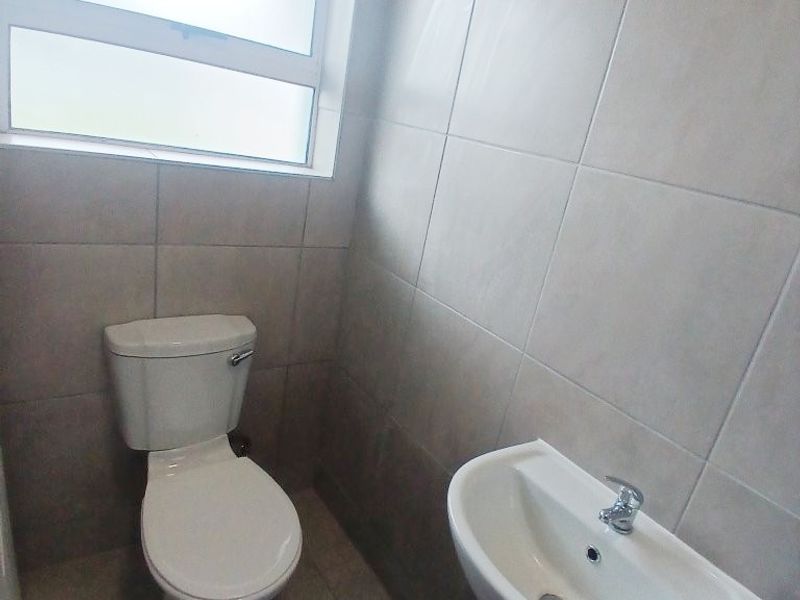 A compact, tiled bathroom featuring a white pedestal basin and a standard toilet, illuminated by a frosted glass window.