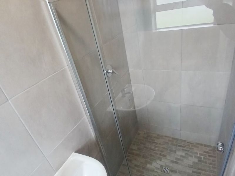 A clean, modern bathroom featuring a pedestal basin and a glass-enclosed shower with neutral wall tiling and a mosaic-tiled shower floor.