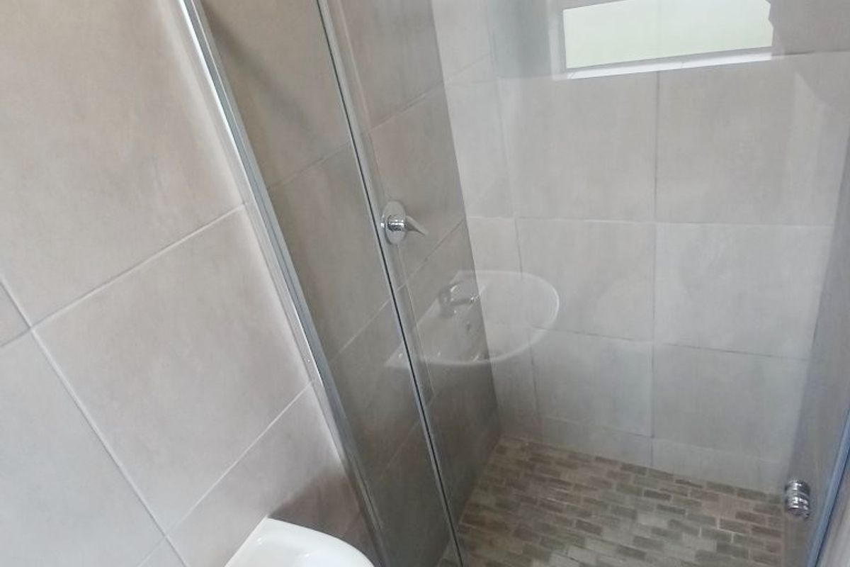 A clean, modern bathroom featuring a pedestal basin and a glass-enclosed shower with neutral wall tiling and a mosaic-tiled shower floor.