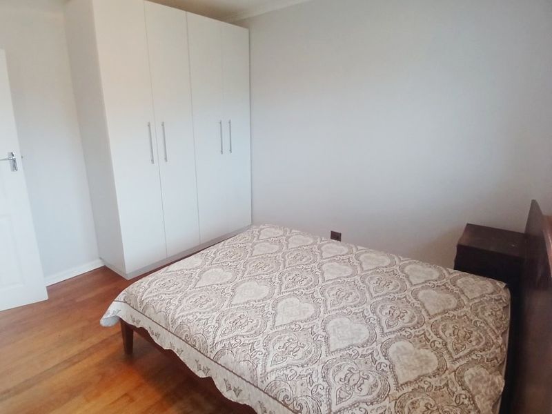 A well-maintained bedroom featuring polished hardwood flooring and a spacious white built-in wardrobe with modern handles.