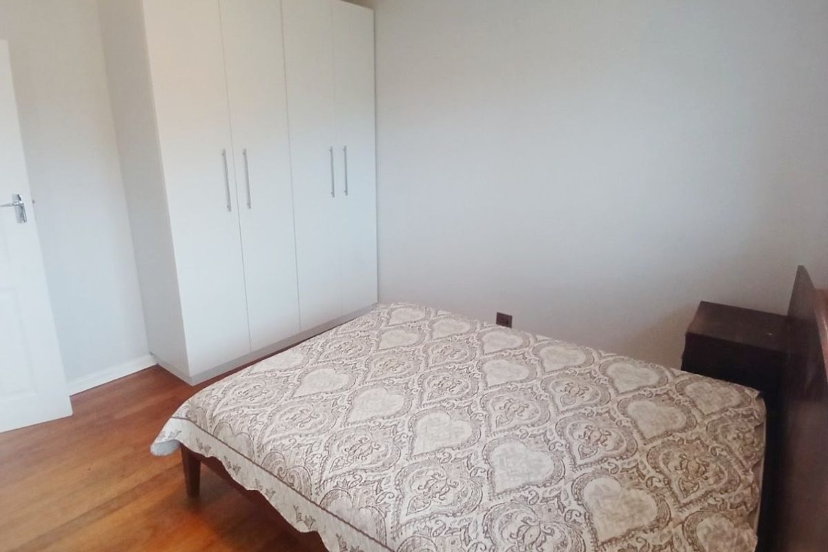 A well-maintained bedroom featuring polished hardwood flooring and a spacious white built-in wardrobe with modern handles.