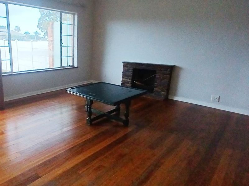Spacious living room featuring polished hardwood flooring, a stone-clad fireplace, and large windows providing natural light.